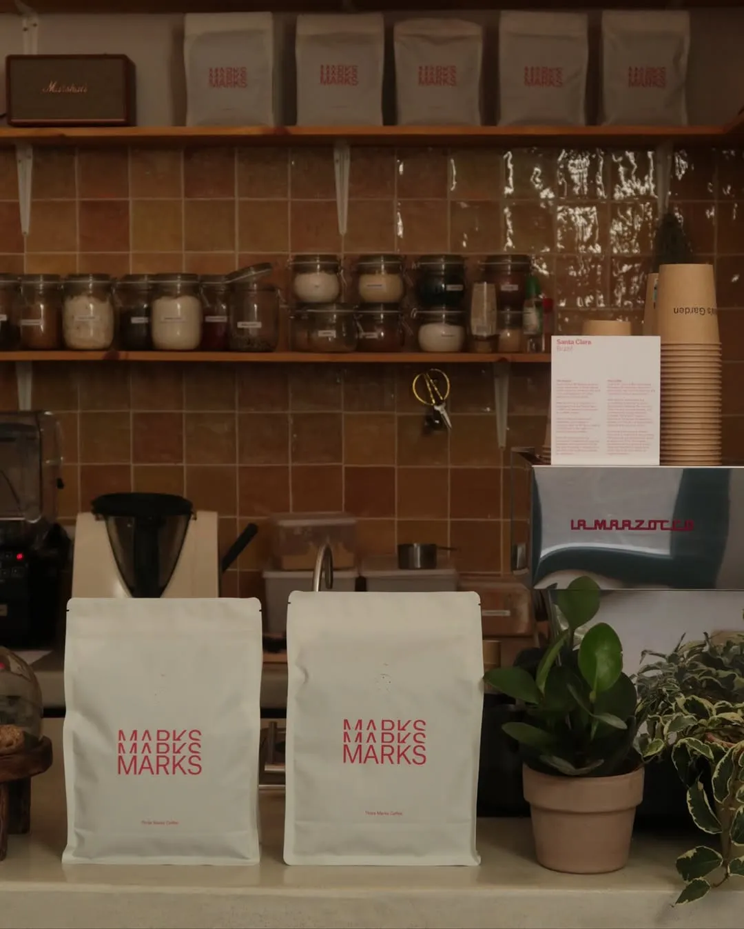 Estantería del local con bolsas de café Three Marks y plantas